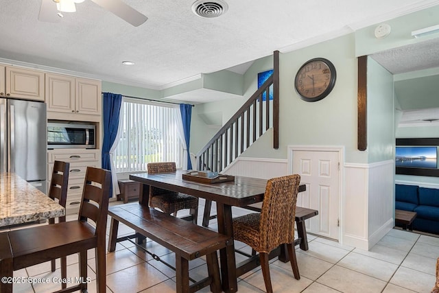 dining area with visible vents, ceiling fan, light tile patterned floors, wainscoting, and a textured ceiling