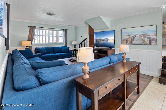 living area featuring visible vents, ornamental molding, a textured ceiling, stairway, and wainscoting