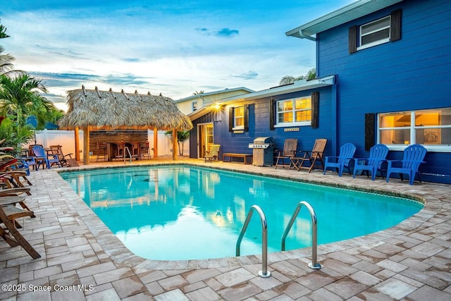 pool at dusk with a fenced in pool, a patio area, fence, and outdoor dry bar