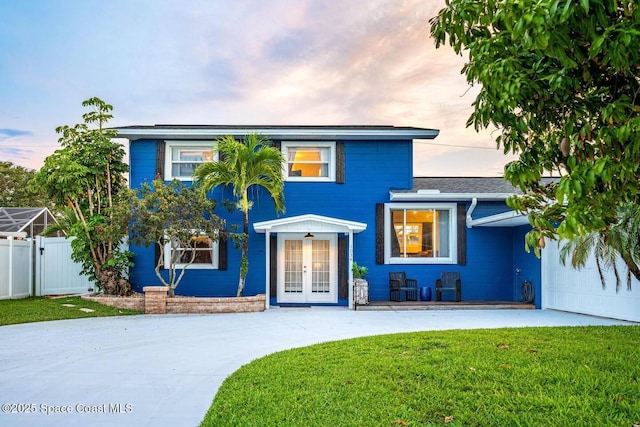 traditional-style home with a front lawn, driveway, fence, french doors, and an attached garage