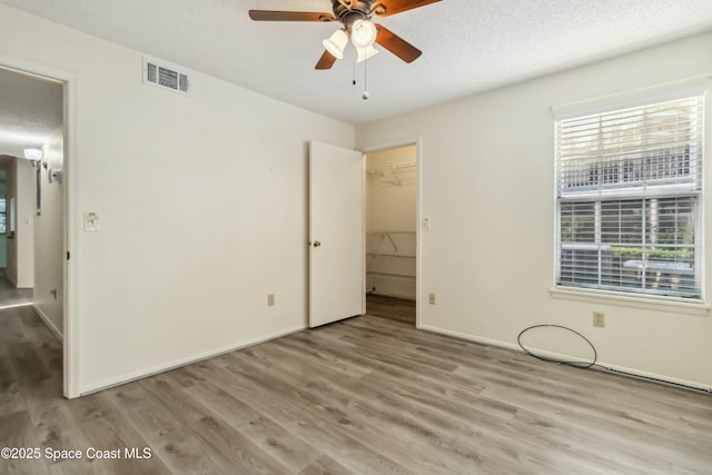 unfurnished bedroom featuring wood finished floors, baseboards, visible vents, a textured ceiling, and a walk in closet