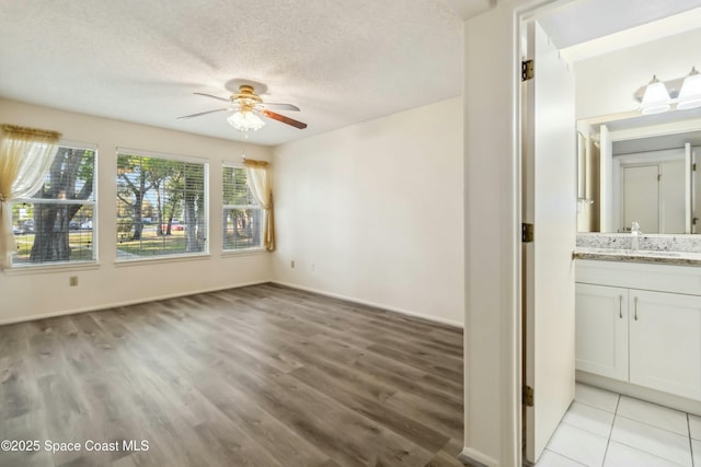 unfurnished room featuring baseboards, light wood finished floors, a sink, ceiling fan, and a textured ceiling