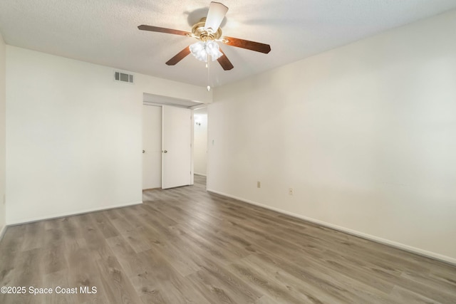 empty room featuring ceiling fan, visible vents, baseboards, and wood finished floors