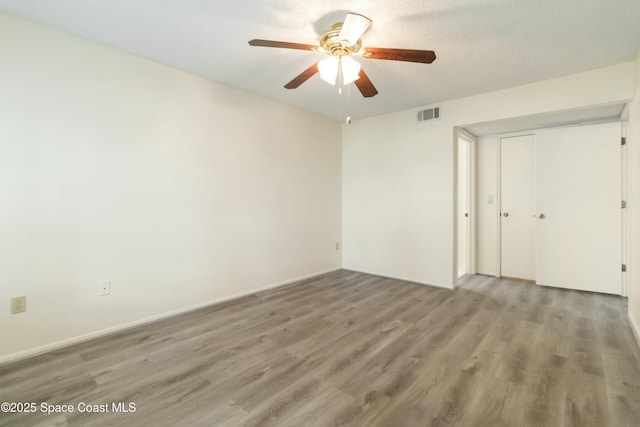 spare room featuring visible vents, a textured ceiling, wood finished floors, baseboards, and ceiling fan