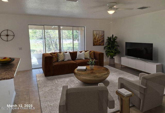 living room featuring light tile patterned floors, a ceiling fan, visible vents, and a textured ceiling