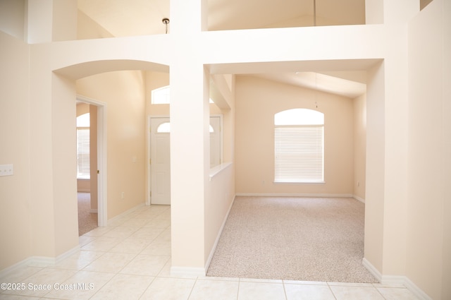 carpeted empty room with tile patterned floors, a healthy amount of sunlight, baseboards, and a towering ceiling