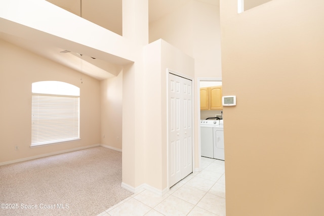 corridor with light carpet, separate washer and dryer, light tile patterned flooring, baseboards, and a towering ceiling