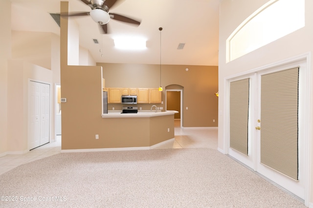 unfurnished living room with light tile patterned floors, light colored carpet, a high ceiling, and a ceiling fan