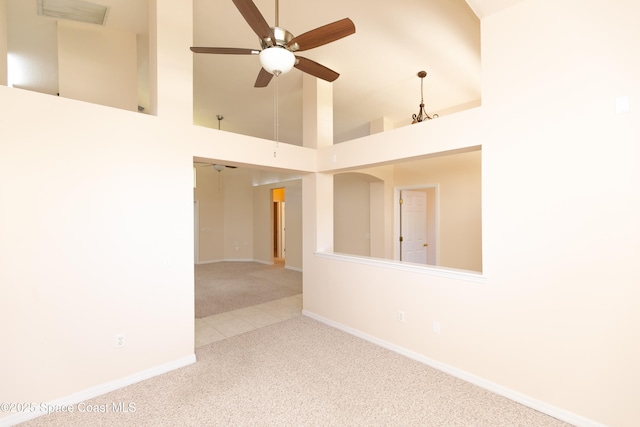 carpeted empty room with a high ceiling, a ceiling fan, visible vents, and baseboards