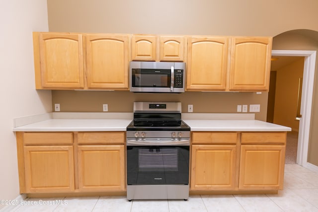 kitchen with light brown cabinets, baseboards, light countertops, arched walkways, and stainless steel appliances