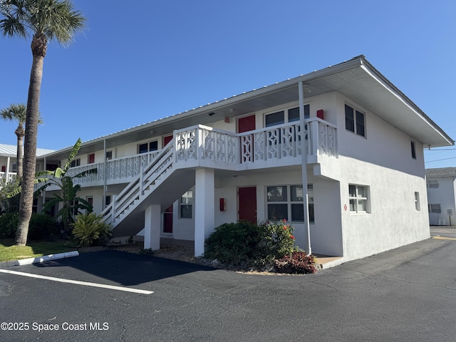 view of front of house featuring stairway, uncovered parking, and stucco siding