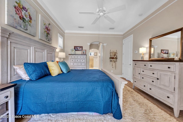 bedroom featuring a ceiling fan, wood finished floors, visible vents, arched walkways, and crown molding