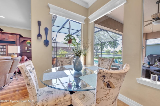 dining space with light wood-style flooring, ornamental molding, a ceiling fan, a sunroom, and baseboards