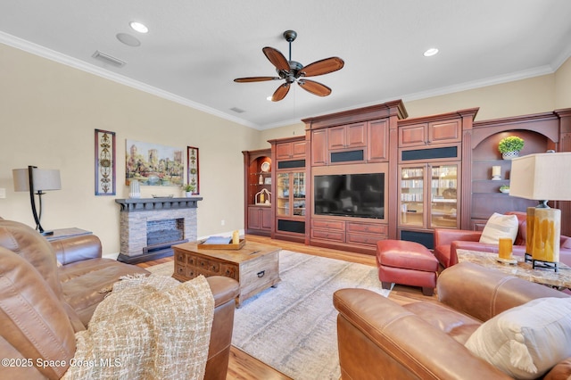 living room featuring ceiling fan, light wood-style flooring, a fireplace, and ornamental molding