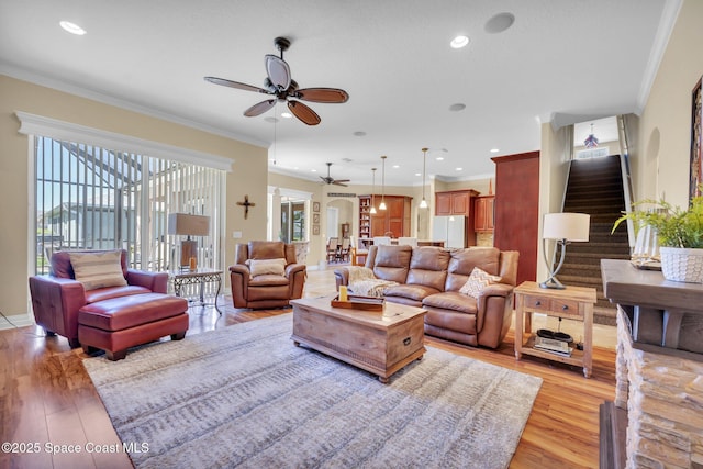 living room with stairway, ceiling fan, crown molding, and light wood-style floors