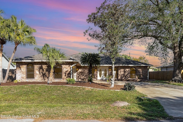 view of front of home with brick siding, driveway, a front yard, and fence