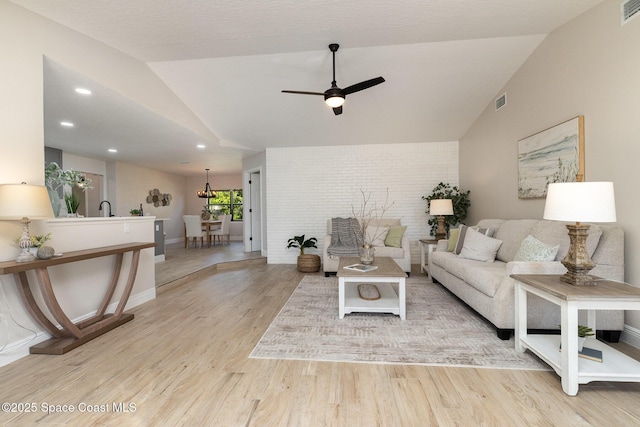 living area with lofted ceiling, wood finished floors, visible vents, and brick wall