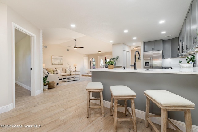 kitchen featuring light countertops, a breakfast bar area, stainless steel fridge, and vaulted ceiling