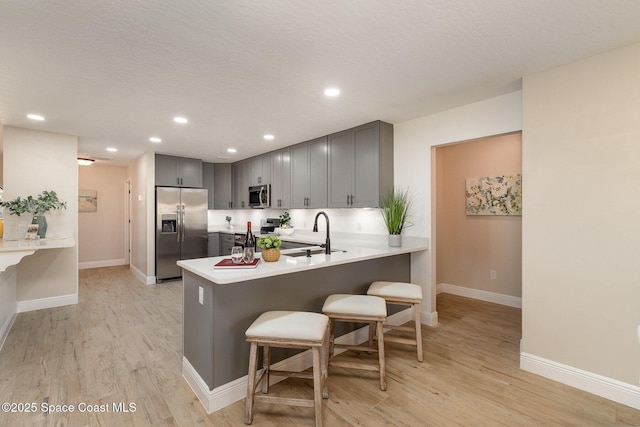 kitchen with gray cabinetry, a breakfast bar area, a peninsula, appliances with stainless steel finishes, and a sink