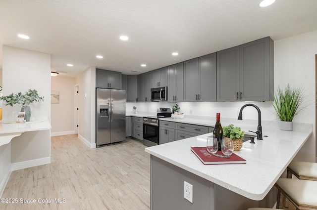 kitchen with gray cabinets, a peninsula, light wood-style flooring, a kitchen breakfast bar, and stainless steel appliances