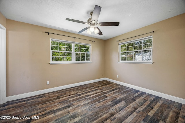 empty room featuring dark wood-style floors, a healthy amount of sunlight, a textured ceiling, and baseboards