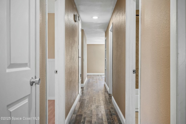 hall with dark wood finished floors and a textured wall