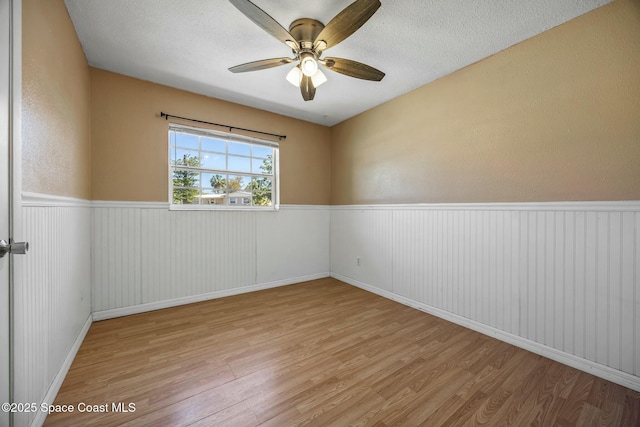 empty room featuring a ceiling fan, a textured ceiling, wood finished floors, and wainscoting