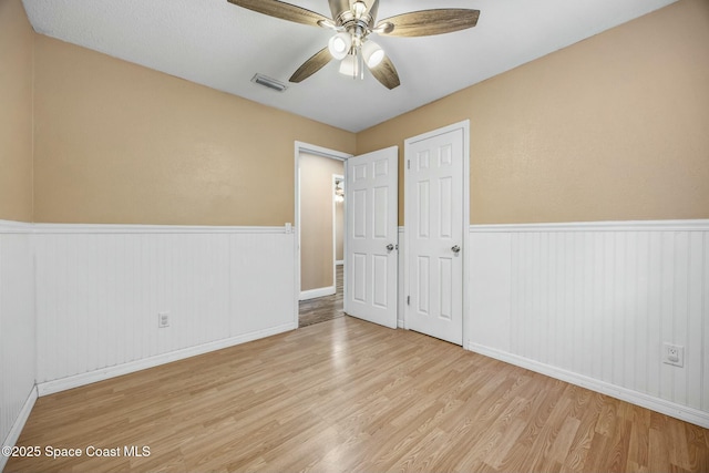 unfurnished bedroom with visible vents, a ceiling fan, a wainscoted wall, and wood finished floors