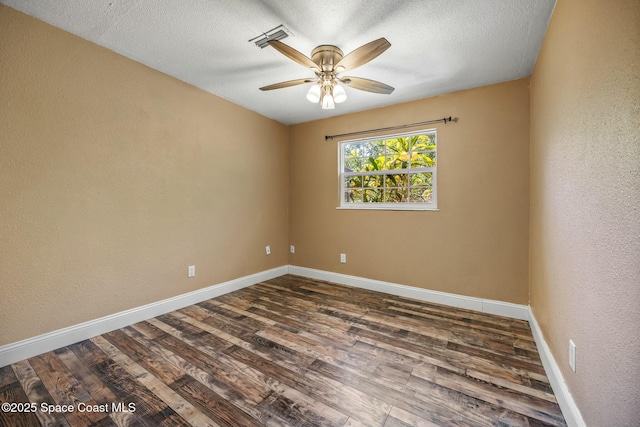 empty room featuring visible vents, dark wood-type flooring, and baseboards