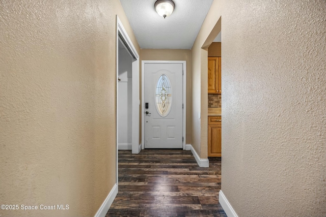 entryway featuring a textured ceiling, a textured wall, dark wood-style flooring, and baseboards