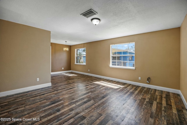 empty room featuring visible vents, a textured ceiling, an inviting chandelier, baseboards, and dark wood-style flooring