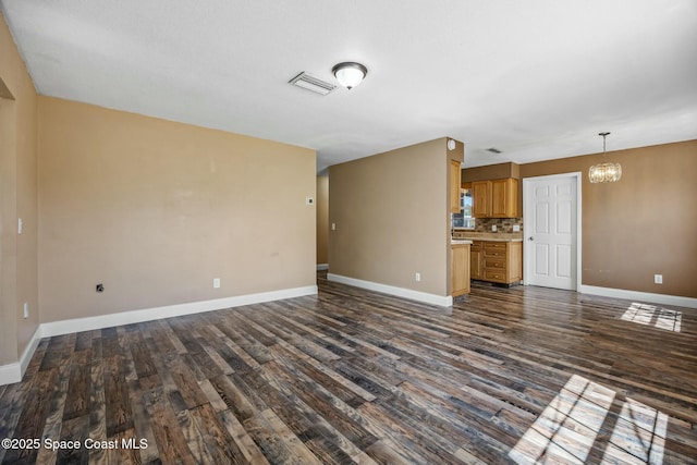 unfurnished living room with an inviting chandelier, baseboards, dark wood-type flooring, and visible vents