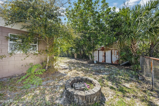 view of yard featuring an outbuilding, a fire pit, fence, and a shed