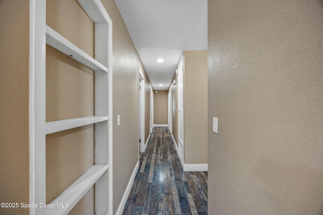 hallway with baseboards, wood finished floors, and a textured wall