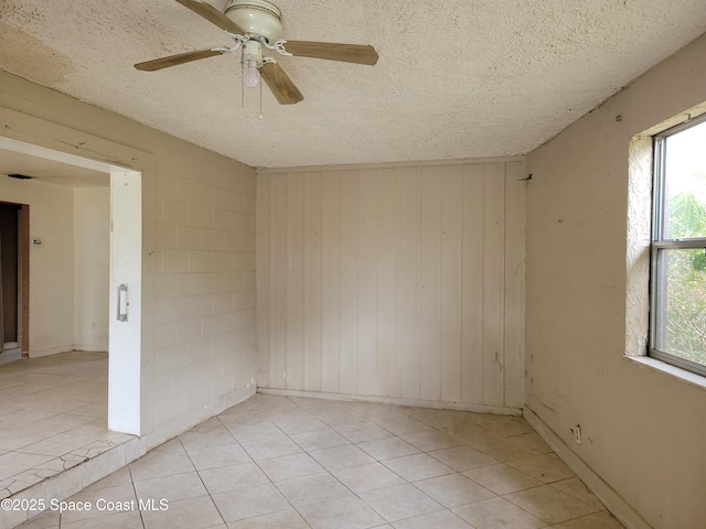 unfurnished room featuring light tile patterned floors, a textured ceiling, concrete block wall, and a ceiling fan