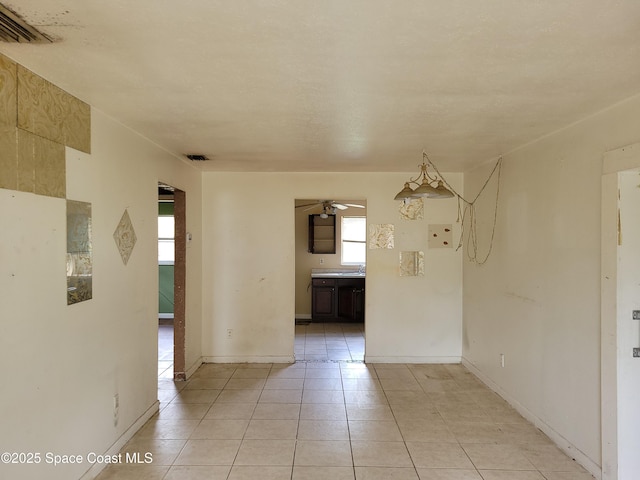 empty room with light tile patterned floors, a ceiling fan, visible vents, and baseboards