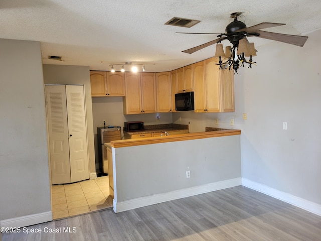 kitchen featuring visible vents, black microwave, light brown cabinetry, light wood-style floors, and a textured ceiling