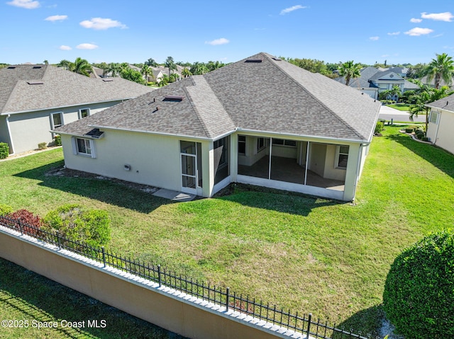 rear view of house featuring fence, roof with shingles, stucco siding, a lawn, and a sunroom