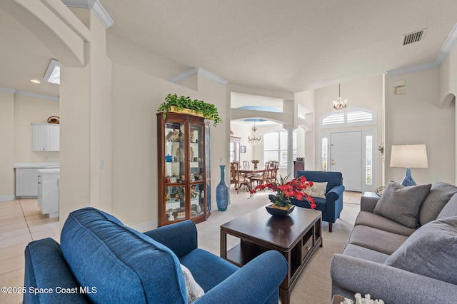 living room with visible vents, ornamental molding, arched walkways, light tile patterned floors, and a chandelier