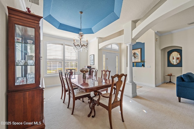 dining area with crown molding, a tray ceiling, decorative columns, light carpet, and arched walkways