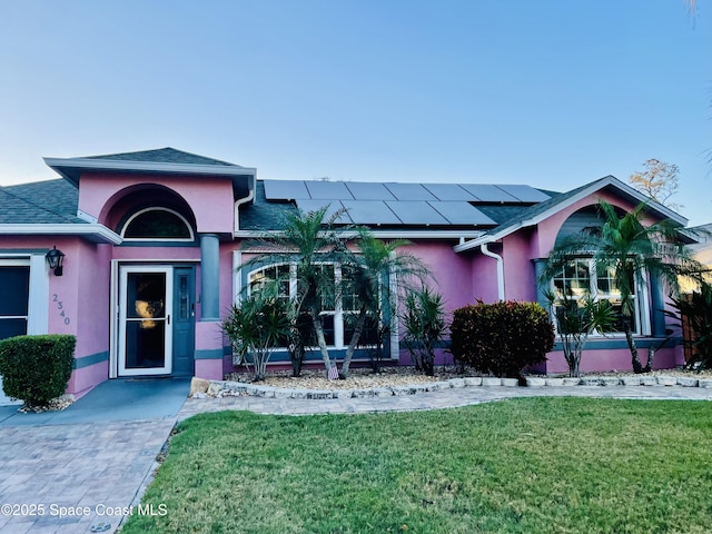 view of front of property featuring a front yard, roof with shingles, roof mounted solar panels, and stucco siding