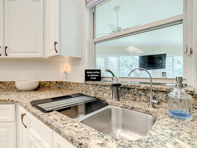 kitchen with white cabinets, light stone counters, and a sink