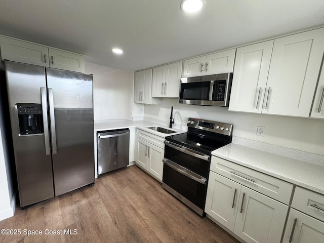 kitchen with wood finished floors, a sink, light countertops, appliances with stainless steel finishes, and white cabinetry