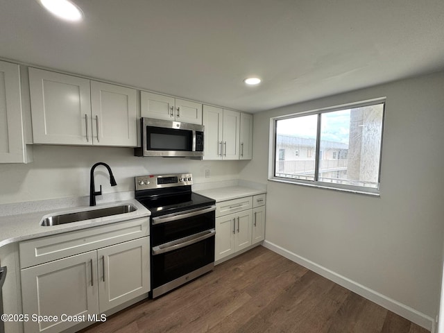 kitchen with dark wood-style floors, a sink, stainless steel appliances, light countertops, and white cabinetry