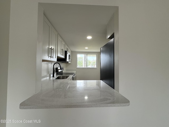 kitchen with light stone countertops, recessed lighting, stainless steel appliances, white cabinetry, and a sink