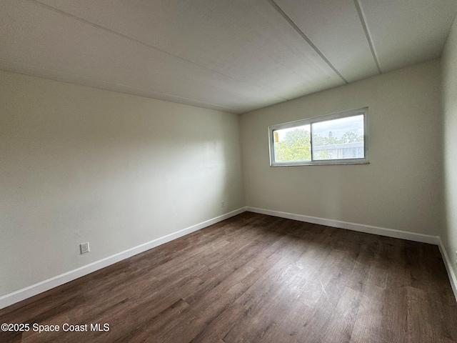 spare room featuring baseboards and dark wood-style floors