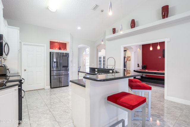 kitchen with a breakfast bar, arched walkways, vaulted ceiling, appliances with stainless steel finishes, and dark countertops