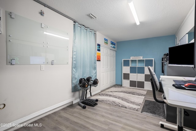 office space with visible vents, a textured ceiling, baseboards, and wood finished floors