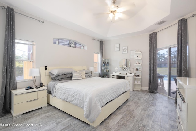 bedroom with access to exterior, visible vents, light wood finished floors, a raised ceiling, and a ceiling fan