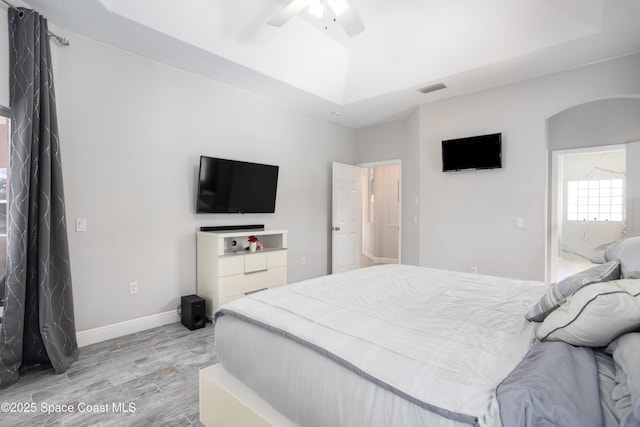 bedroom with a ceiling fan, baseboards, visible vents, light wood-style flooring, and a raised ceiling